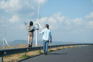 zurück Aussicht von jung Paar Gehen auf das Straße mit Wind Turbinen im Hintergrund foto