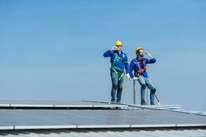 beide von Techniker reparieren Solar- Paneele sich ausruhen im das sengend Sonne auf ein Fabrik Dach bedeckt mit Solar- Paneele zu erhalten Solar- Energie. foto