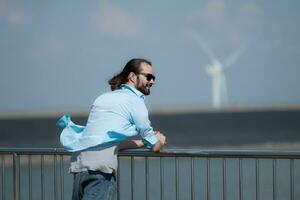 jung Mann entspannend durch das Wind Turbine auf das See foto