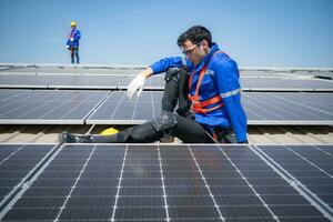 Techniker reparieren Solar- Paneele nehmen aus seine Hut und sich ausruhen im das sengend Sonne auf ein Fabrik Dach bedeckt mit Solar- Paneele zu erhalten Solar- Energie. foto