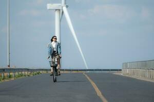 jung Frau Reiten ein Fahrrad auf ein Straße im ein Windmühle. foto