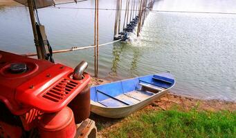 Motor- Motor mit Boot und Belüfter mehrere Turbine Räder auf Wasser Oberfläche zum erhöhen, ansteigen Sauerstoff im Garnele Teich und natürlich Bauernhof Hintergrund foto