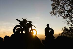Mann mit Moto-Cross Fahrrad gegen schön Beleuchtung, Silhouette von ein Mann mit Moto-Cross Motorrad auf oben von Felsen hoch Berg beim schön Sonnenuntergang, Enduro Motorrad Reise Konzept. foto