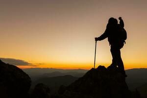 Silhouette von ein Wanderer Mann auf ein Felsen Sockel mit Hände hoch. schön Orange Sonnenuntergang. unabhängig Wandern reisen, Erfolg. foto