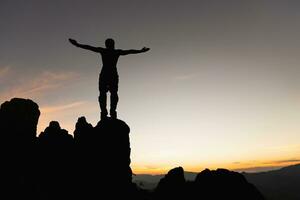 Silhouette von Mann steigend Hände beim Gipfel von Berge. erfolgreich erreichen Ihre Ziel. Erfolg Geschäft Führung, erfolgreich Person hat erreichen. foto