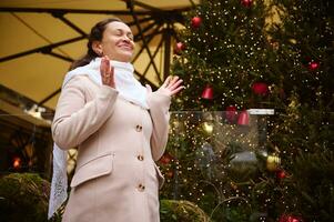 ziemlich Frau Herstellung geschätzt Wunsch, Stehen durch ein Weihnachten Baum dekoriert zum Weihnachten im das Stadt Platz foto