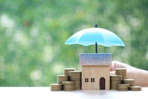 Schutz, Modell- Haus und Stapel von Münzen Geld mit das Regenschirm auf Natur Grün Hintergrund, Finanzen Versicherung und sicher Investition Konzept foto