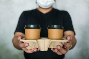 Kellnerin tragen ein Gesicht Maske Handhabung zwei heiß Kaffee Tasse zu ein Kunde. foto