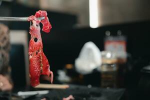 Heben ein Scheibe von ein gegrillt Prämie Rindfleisch beim ein Yakiniku Restaurant durch mit Essstäbchen foto
