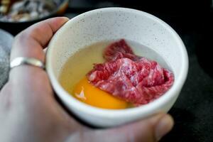 Prämie frisch Rindfleisch stellen im roh Eigelb Ei im Weiß Schüssel zum gekocht japanisch Sukiyaki foto