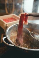 Eintauchen ein geschnitten Stück von Schweinefleisch in Wasser heiß Topf während Essen Shabu oder Sukiyaki Mahlzeit. foto