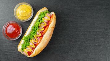hausgemacht heiß Hund mit Senf, Ketchup, Tomate und frisch Salat Blätter auf schwarz Schiefer Hintergrund foto