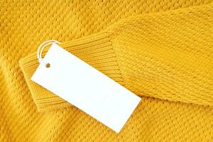 weißes leeres rechteckiges Kleidungsetikett auf gelbem Strickpullover isoliert auf weißem Hintergrund foto