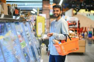 Porträt von glücklich indisch Mann Stehen im Vorderseite von das Produkt Zähler im ein Lebensmittelgeschäft speichern. Mann Kauf Lebensmittelgeschäft zum Zuhause im Supermarkt. foto