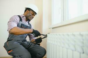 afro Handwerker im Overall mit Werkzeuge während Installation oder reparieren Heizung Kühler foto