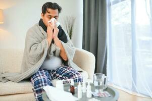 Porträt von krank indisch Mann mit flüssig Nase halten Papier Servietten in der Nähe von Gesicht Sitzung beim heim. Grippe, Virus, Allergie Konzept foto