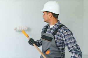 ein indisch Wohnung Reparatur Arbeiter Farben ein Weiß Mauer mit ein Rolle. foto