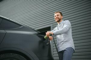Mann halten Leistung Laden Kabel zum elektrisch Auto im draussen Auto Park foto