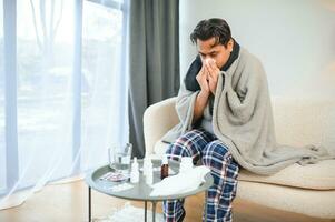 Porträt von krank indisch Mann mit flüssig Nase halten Papier Servietten in der Nähe von Gesicht Sitzung beim heim. Grippe, Virus, Allergie Konzept foto