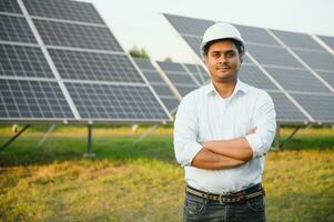 Porträt von jung indisch männlich Ingenieur Stehen in der Nähe von Solar- Tafeln, mit klar Blau Himmel Hintergrund, verlängerbar und sauber Energie. Fertigkeit Indien, Kopieren Raum foto