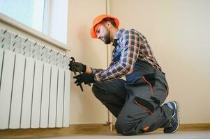 jung Mann Klempner Überprüfung Kühler während Installation Heizung System im Wohnung foto