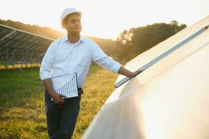 Porträt von jung indisch männlich Ingenieur Stehen in der Nähe von Solar- Tafeln, mit klar Blau Himmel Hintergrund, verlängerbar und sauber Energie. Fertigkeit Indien, Kopieren Raum foto