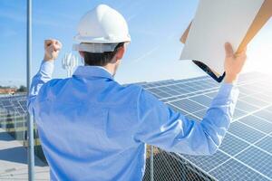 glücklich Ingenieur im schützend Helm auf ein Solar- Leistung Pflanze feiern Erfolg. foto