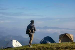 Reisender ist Trekking zu das Berg oben beim Campingplatz mit mehrere Zelte unter das schön szenisch von hoch Höhe Aussicht zum draussen Abenteuer Ferien Reise foto