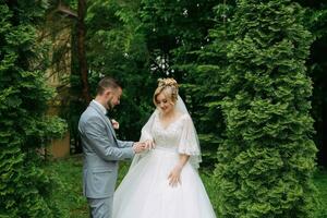 Porträt von das Braut und Bräutigam Stehen gegen das Hintergrund von Grün Bäume, das Bräutigam Putten auf das Braut Hochzeit Ring. stilvoll Bräutigam. Mode und Stil. foto