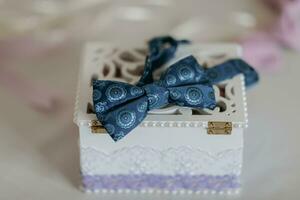 das Bräutigam Blau Schmetterling ist Stehen auf ein hölzern Box mit Hochzeit Ringe auf ein Weiß Hintergrund. Hochzeit Einzelheiten. Stil. foto