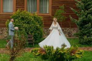 Hochzeit im Natur. Foto von das Braut und Bräutigam auf ein gehen gegen das Hintergrund von Bäume, das Braut geht zu Treffen das Bräutigam, gegen das Hintergrund von Bäume und ein hölzern Hütte. stilvoll Bräutigam.