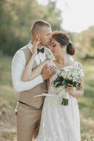 Hochzeit Foto im Natur. das Braut und Bräutigam sind Stehen im das Wald, das Bräutigam Umarmungen seine Geliebte von hinter und Küsse ihr, sie lächelt aufrichtig. Porträt. Sommer- Hochzeit