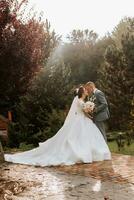 gut aussehend Bräutigam und charmant Braut zusammen im das Park. Porträt. luxuriös Kleid mit ein lange Zug. elegant jung Bräutigam. Hochzeit Strauß. Luxus Hochzeit Platz zum Unterschrift foto