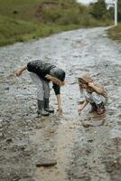 zwei glücklich wenig Mädchen von europäisch Aussehen spielen im Pfützen während Regen im Sommer. Kinder sind spielen im das Regen. Kind spielen im Natur draußen. das Mädchen genießt das Regen. foto