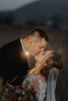 schön Braut und Bräutigam im Abend Beleuchtung, küssen und umarmen halten ein Strauß von Blumen foto