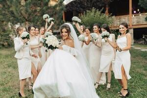 Hochzeit Foto im Natur. ein Brünette Braut im ein lange Weiß Kleid steht im Vorderseite von ihr freunde im nackt Kleider, Wer Stand lächelnd, halten oben ihr Gypsophila Blumensträuße. jung Frauen. Emotionen
