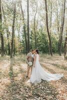 Hochzeit Foto. das Braut und Bräutigam Stand zärtlich küssen im das Wald. lange Zug von ein Hochzeit Kleid. Paar im Liebe. Sommer- Licht. das Schatten foto