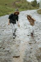 zwei glücklich wenig Mädchen von europäisch Aussehen spielen im Pfützen während Regen im Sommer. Kinder sind spielen im das Regen. Kind spielen im Natur draußen. das Mädchen genießt das Regen. foto