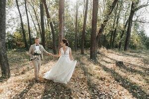 Hochzeit Foto im Natur. das Braut und Bräutigam sind Gehen im das Wald, halten Hände und suchen beim jeder andere, das Braut ist halten ihr Hochzeit Kleid schön. Paar im Liebe. Sommer- Licht.