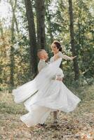 Porträt von glücklich Braut und Bräutigam im das Wald. das Bräutigam hält das Braut im seine Waffen, Tanzen mit ihr. Foto von das Kleid im Bewegung. Hochzeit Foto Session im Natur.