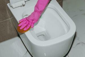 ein Frau reinigt das Toilette mit ein Toilette Gewebe. ein Hausfrau wie ein Toilette Reiniger. sauber das Toilette zum Sauberkeit und Hygiene. Toilette Reinigung Reinigung Bedienung Konzept. Rosa Gummi Handschuh foto