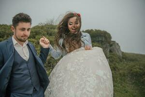 glücklich Hochzeit Paar im das Berge. das Bräutigam führt das Braut unten durch das Hand. sie lächelt aufrichtig. Hochzeit Foto Session im Natur. Foto Session im das Wald von das Braut und Bräutigam.