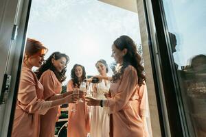 jung Brautjungfern sind haben Spaß und lächelnd im Rosa Seide Roben Trinken Champagner beim das Braut Pavillon. schön Frauen feiern ein Bachelorette Party, im ein Pavillon und mit Champagner. foto