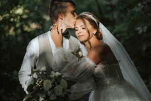 Porträt von ein schön Paar im Liebe auf Ihre Hochzeit Tag. ein gehen im das Park im das Sonnenlicht. tolle Küsse und Umarmungen von das Braut und Bräutigam mit ein Strauß foto