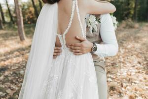 Hochzeit Foto im Natur. das Braut Umarmungen das Bräutigam. Bräutigam Hände auf das Braut Taille. mal schön Schultern von das Braut. Einzelheiten