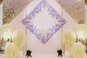 ein groß hell Halle dekoriert mit Weiß Blumen und ein lila Muster zum das Frischvermählte, Hochzeit Tabelle Dekor, das Präsidium von das Jungvermählten foto