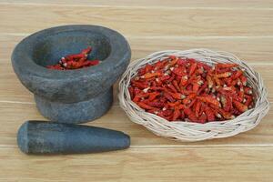 alt Granit Stein Granatwerfer mit Stößel und Korb von rot getrocknet Peperoni zum Kochkonzept, Küche Utensilien .thailändisch Kochen Werkzeug, verwenden zu Pfund Chili Einfügen oder Curry Paste. foto