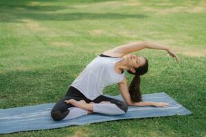 jung Frauen haben ein schön Körper, spielen Yoga im ein elegant Haltung, im das Grün Park, ist ein Konzept von Menschen Erholung und Gesundheit Pflege Konzept. verschwommen Hintergrund foto