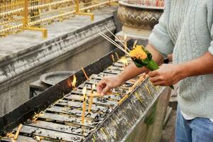 Nahansicht und Ernte Hände von asiatisch Frau halten ein Weihrauch Blume und Kegel und Licht das Kerze zum Anbetung das Buddha beim das thailändisch Tempel auf das Ende von das Jahr. foto