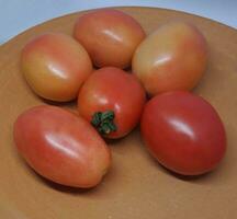 ein Bild von ein Stapel von Tomaten platziert auf ein Lehm Platte. foto